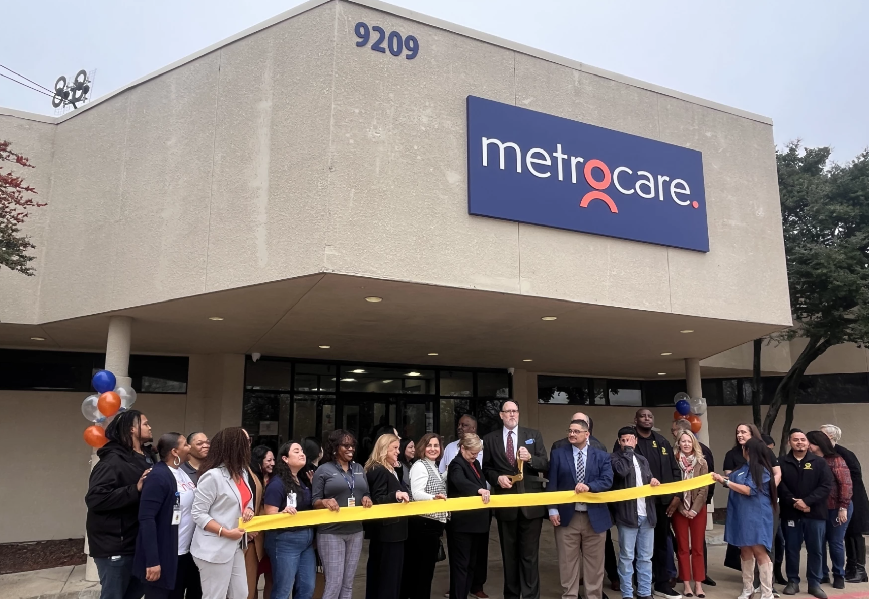 People gathered outside for ribbon cutting with yellow ribbon